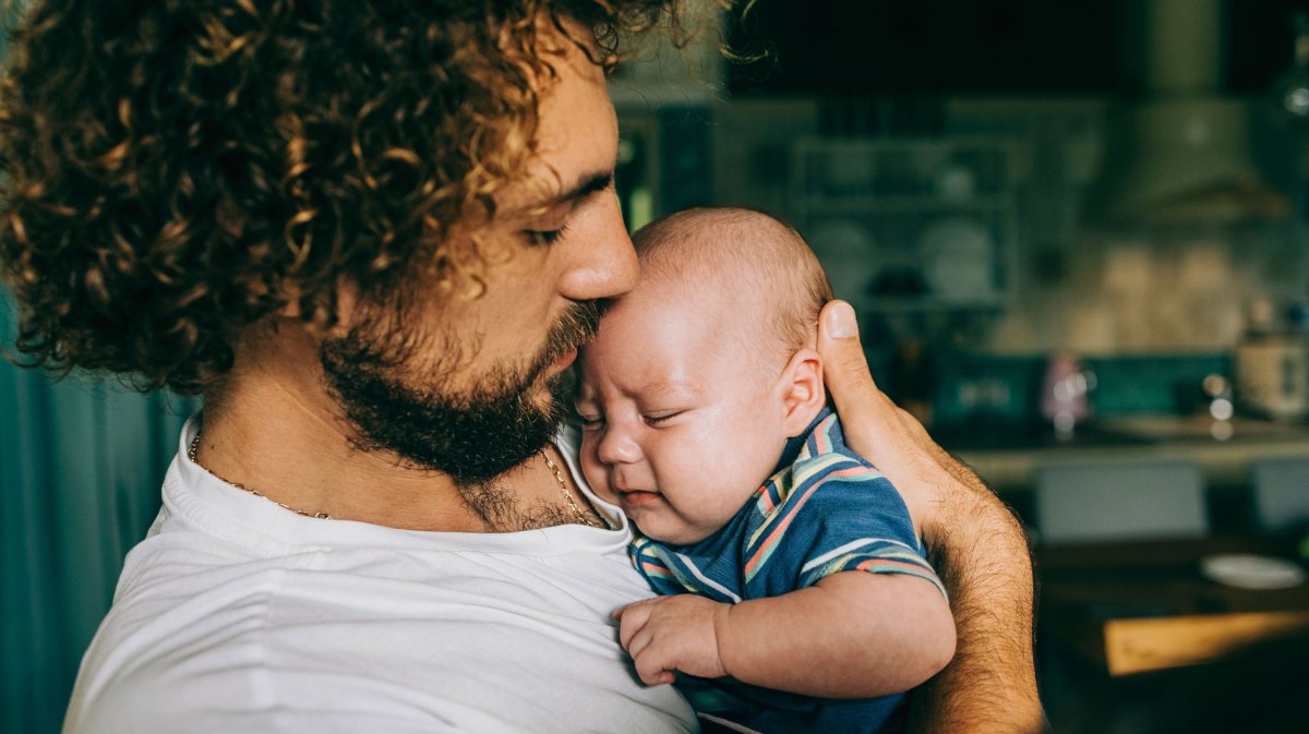 Vater hält sein unzufriedenes Baby etwas hilflos auf dem Arm.