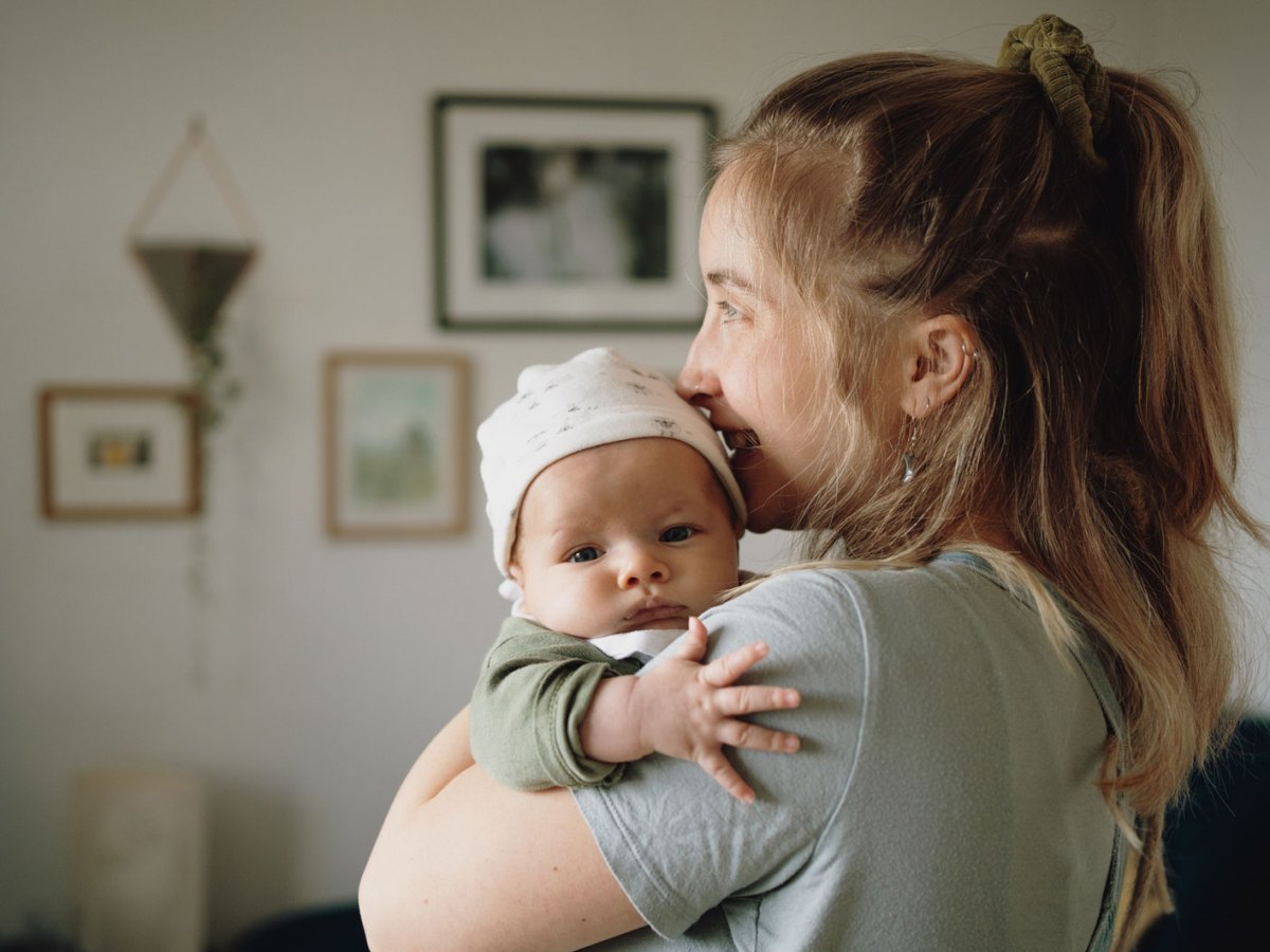 Mutter hält kleines Baby im Arm und schaut aus dem Fenster.