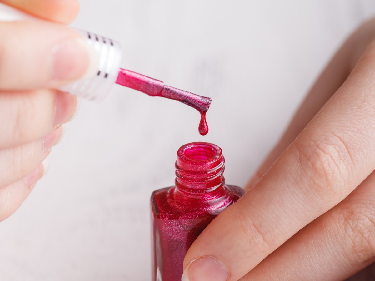 Frau hält Nagellack-Pinsel und Nagellack in der Hand.