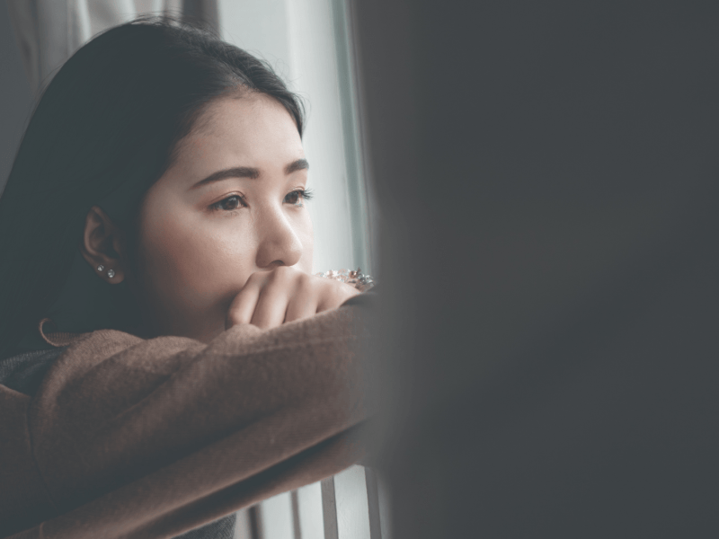 Frau schaut nachdenklich aus dem Fenster
