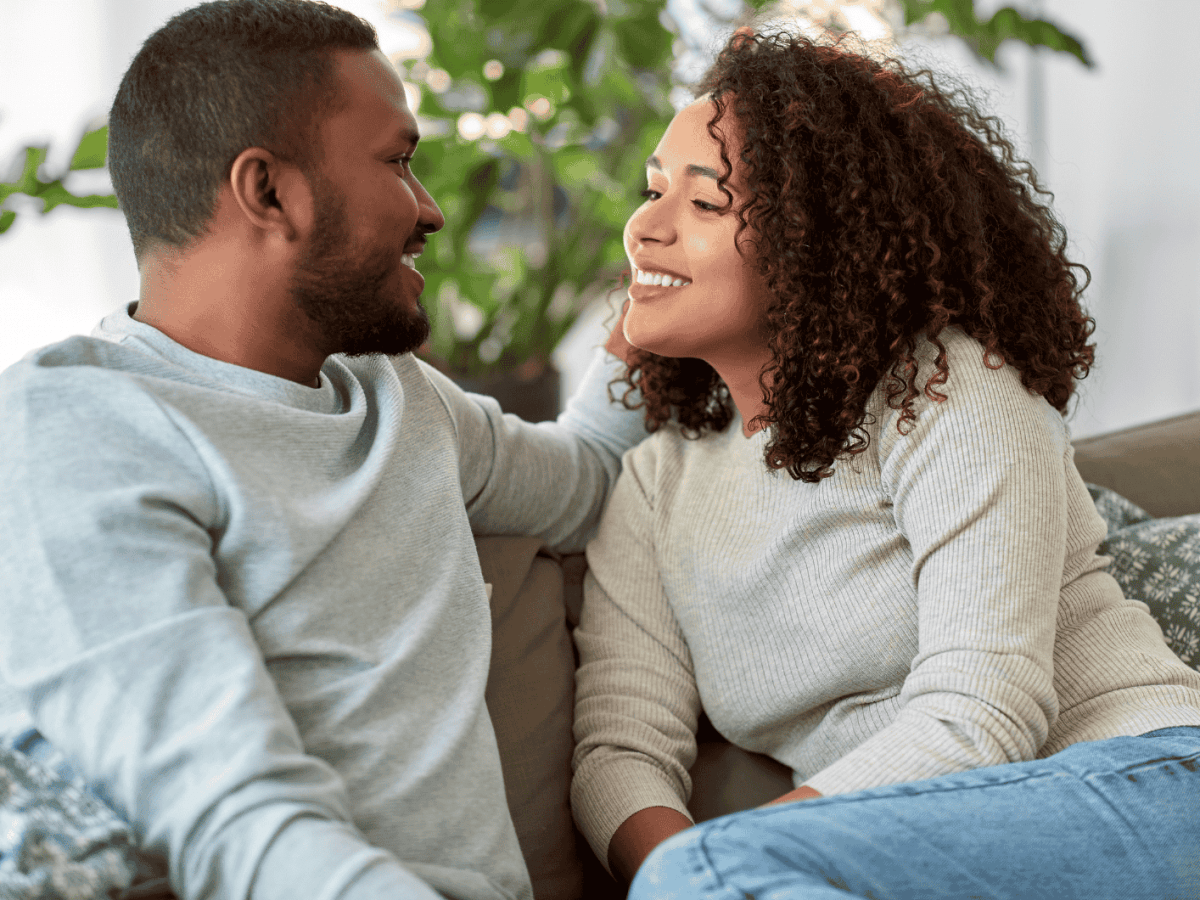 Frau und Mann sitzen auf dem Sofa und l&auml;cheln sich an