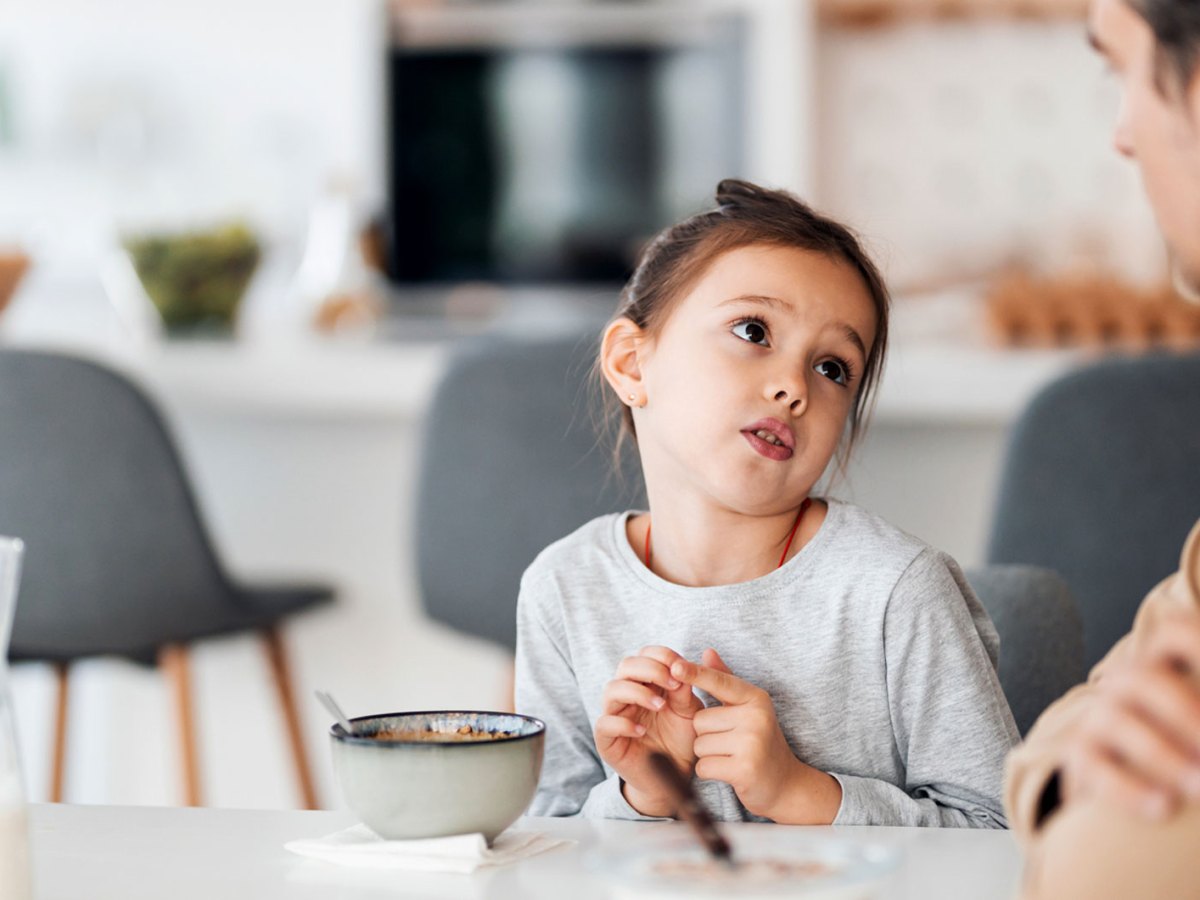M&auml;dchen sitzt mit seinem Vater am Fr&uuml;hst&uuml;ckstisch und bettelt um etwas.