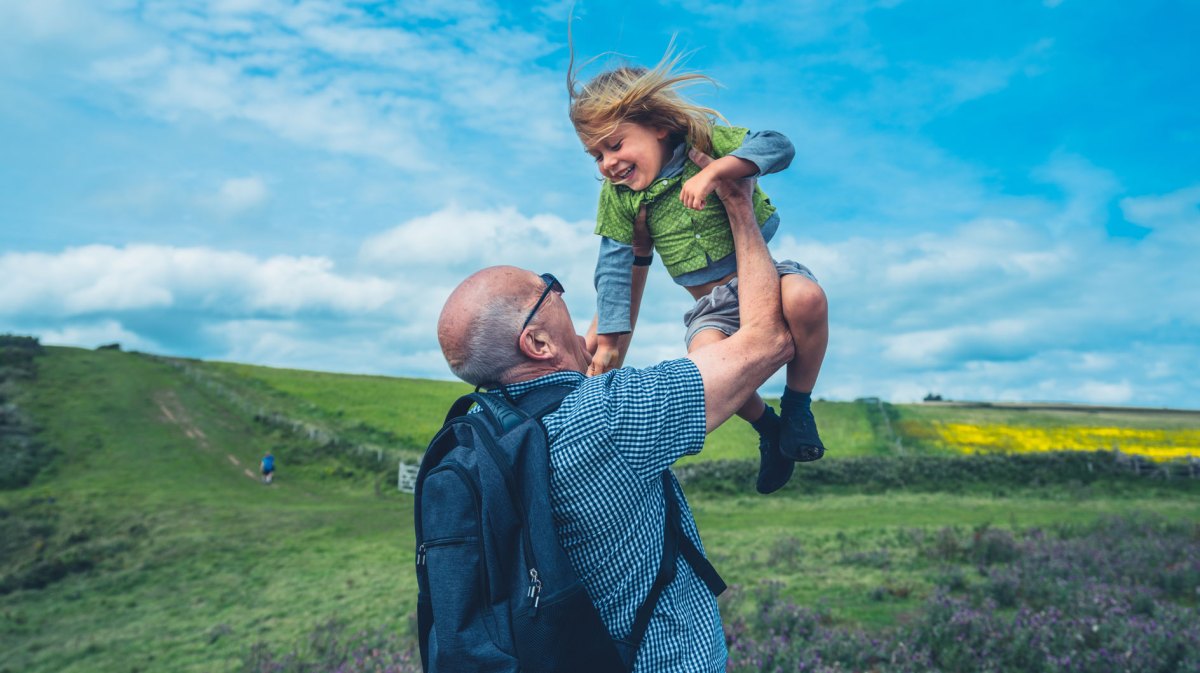 Großvater und Enkel auf einer Wanderung. Der Großvater hebt seinen Enkelsohn in die Luft.