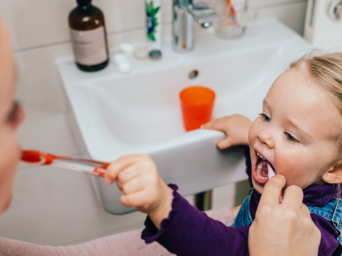 Kleinkind und Mutter putzen sich im Badezimmer gegenseitig die Z&auml;hne