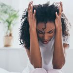 Erschöpfte afroamerikanische Frau leidet unter Kopfschmerzen im Schlafzimmer