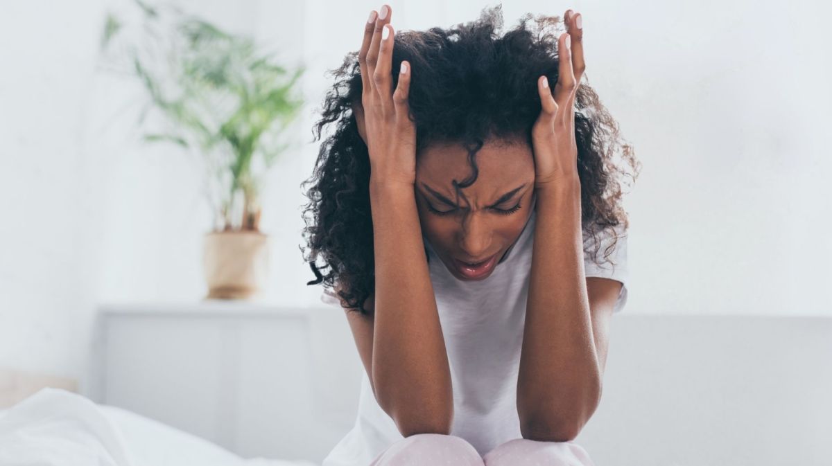 Erschöpfte afroamerikanische Frau leidet unter Kopfschmerzen im Schlafzimmer