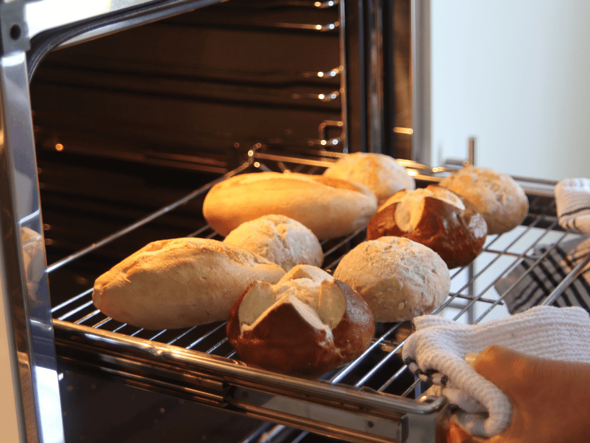 Person schiebt Ofengitter mit Br&ouml;tchen darauf in den Backofen.