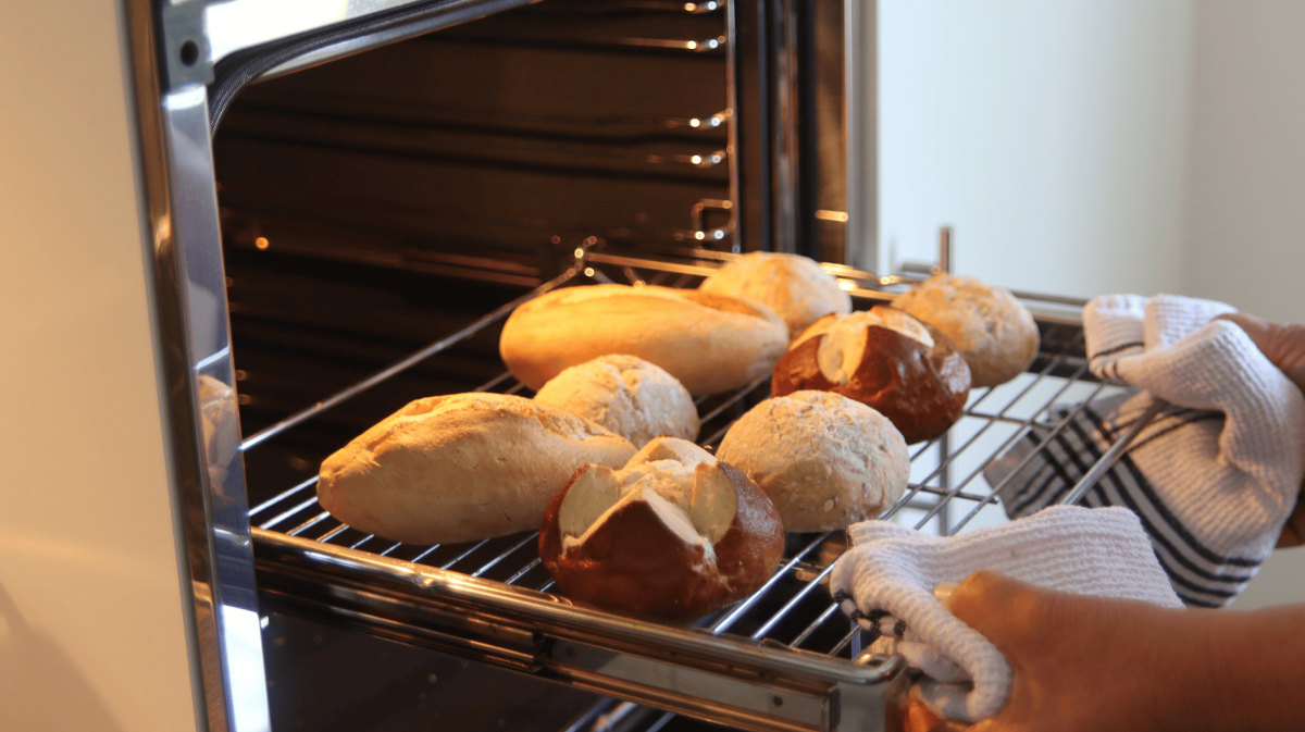 Person schiebt Ofengitter mit Brötchen darauf in den Backofen.