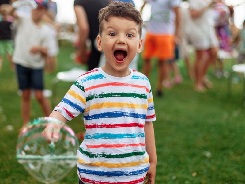 Junge, ca. 5 Jahre alt,an einem Sommerabend im Park, mit einer großen Seifenblase in der Hand.