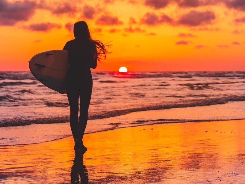 Silhouette der Surferin mit Surfbrett am Strand bei Sonnenuntergang. Surferin und Meer