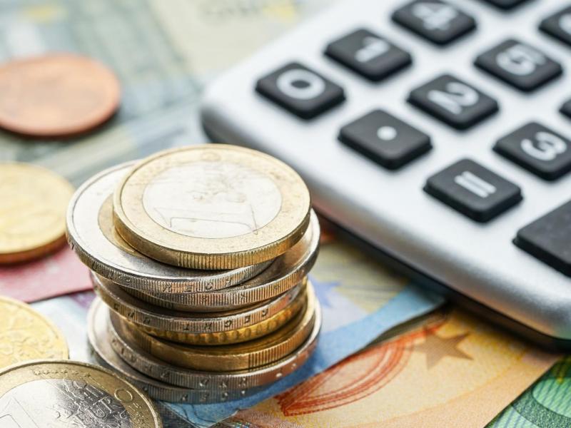 Scheine und Münzgeld liegen gestapelt neben einem Taschenrechner.