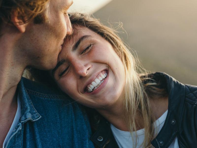 Mann küsst lachende Frau liebevoll auf die Stirn.
