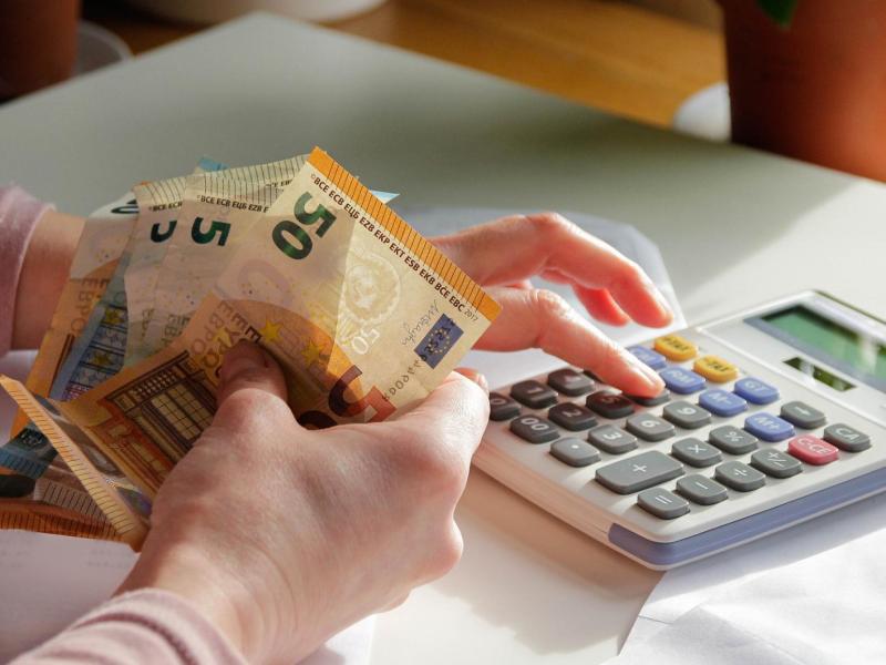 Frau hält Geldscheine in der Hand und tippt auf einem Taschenrechner.