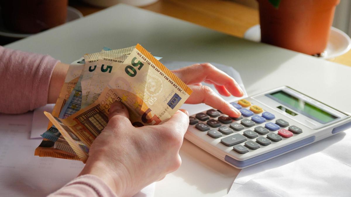 Frau hält Geldscheine in der Hand und tippt auf einem Taschenrechner.
