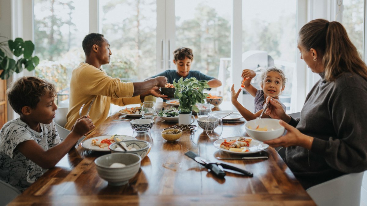 5-köpfige Familie sitzt zusammen am Tisch und isst.