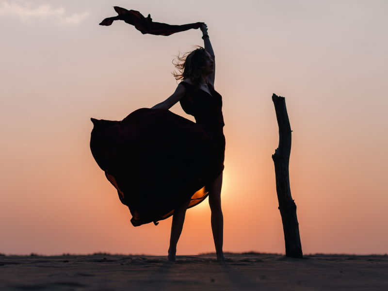 Frau steht vor dem Sonnenuntergang mit einem wehenden Rock
