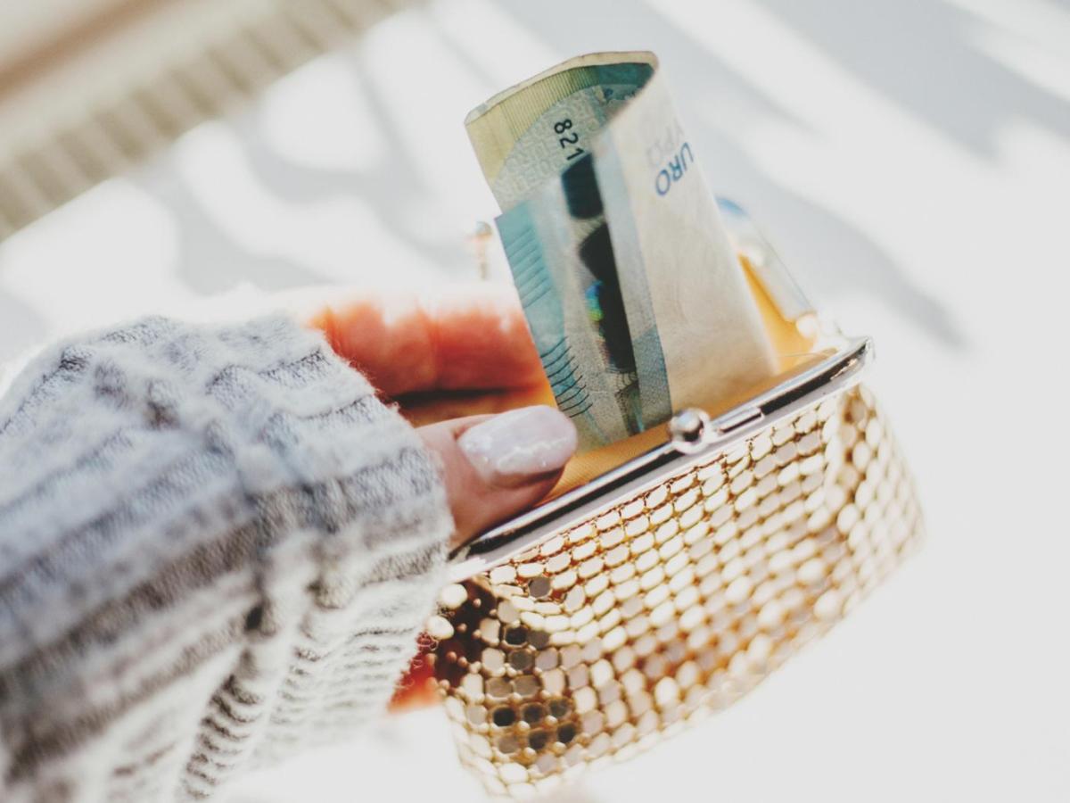 Frau mit künstlichen Gelnägeln hält eine goldene Geldbörse, aus der Geldscheine gucken.