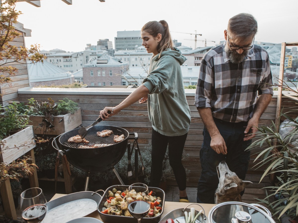 Mann und Frau grillen W&uuml;rstchen auf dem Balkon.