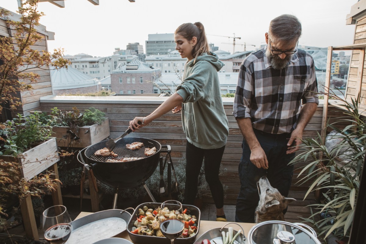 Mann und Frau grillen Würstchen auf dem Balkon.