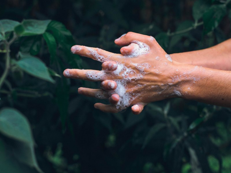 Eingeseifte Hände vor einem grünen Hintergrund.