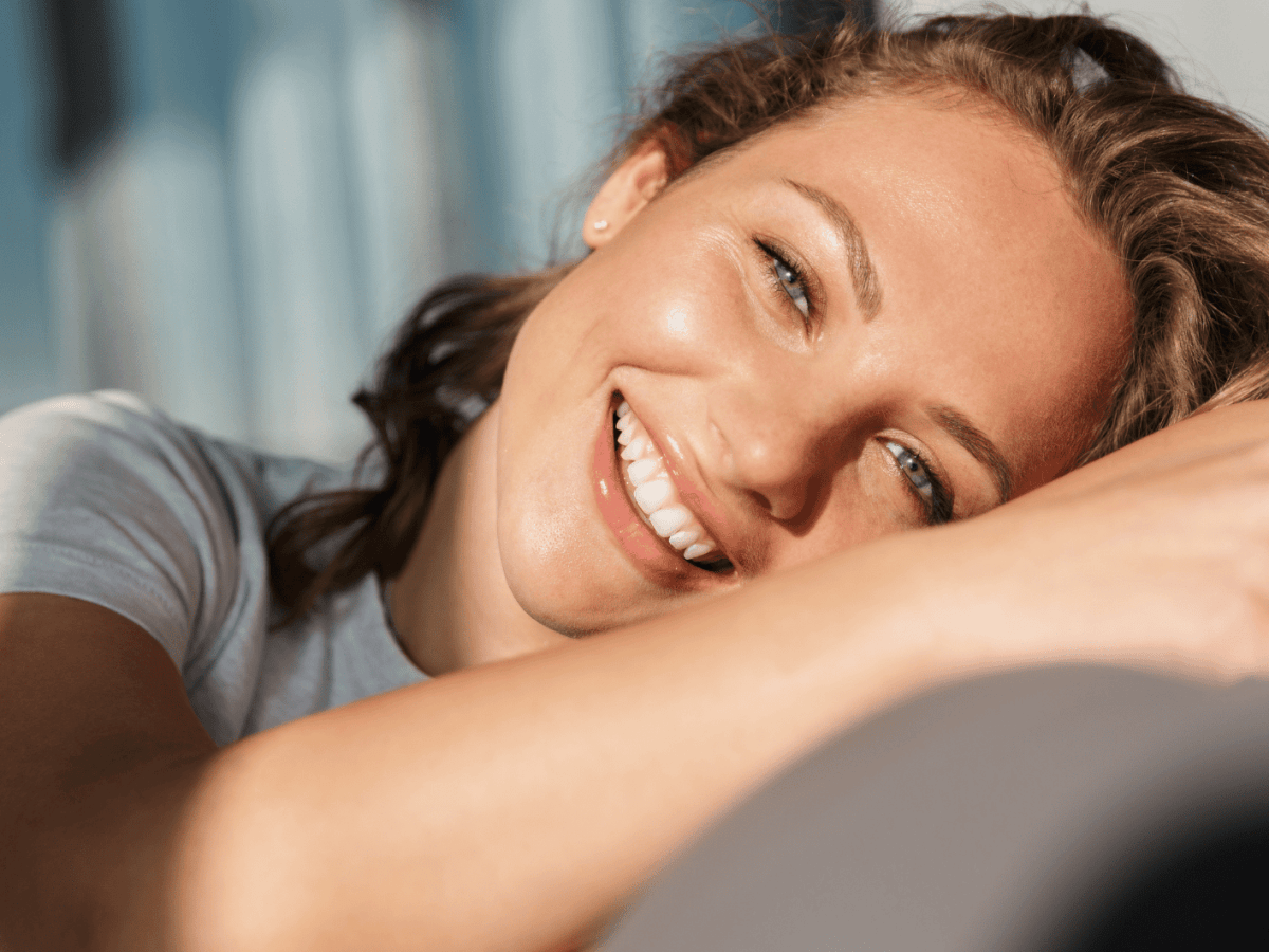 Frau liegt im Sonnenlicht l&auml;chelnd auf einem Sofa