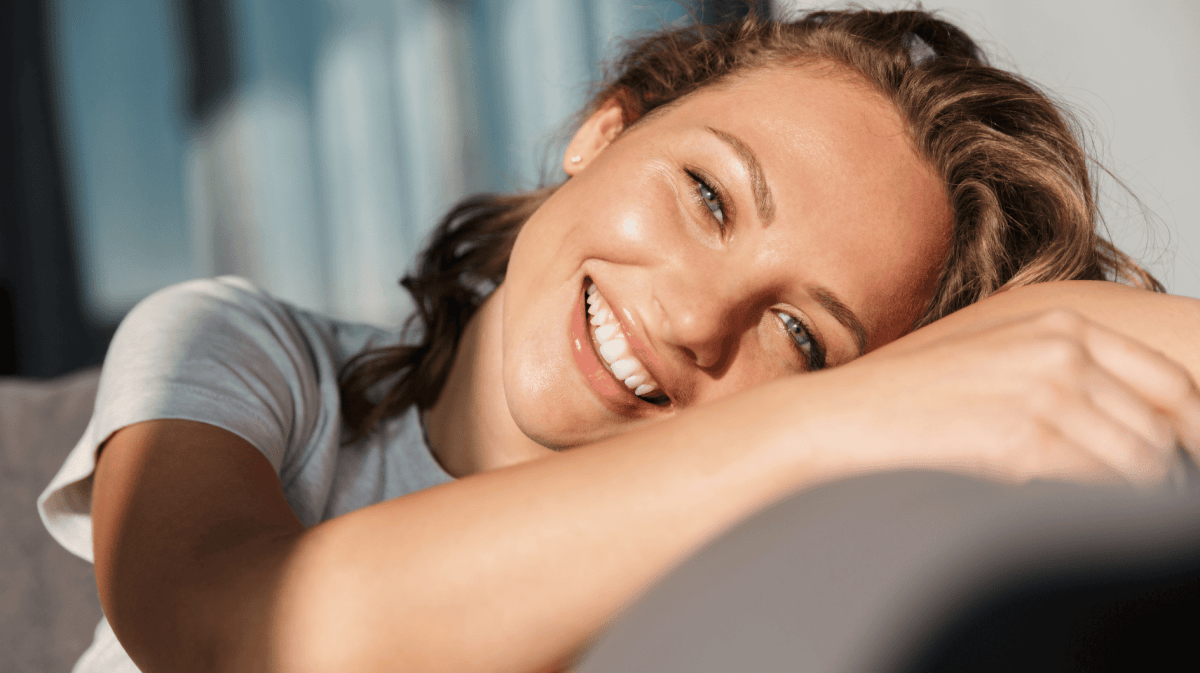 Frau liegt im Sonnenlicht lächelnd auf einem Sofa