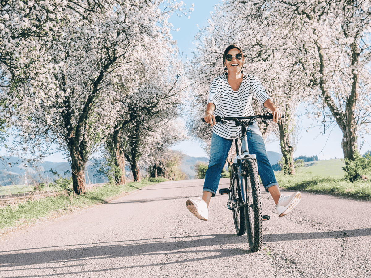 Frau strahlend auf dme Fahrrad umgeben von einer Kirschblütenbaumallee