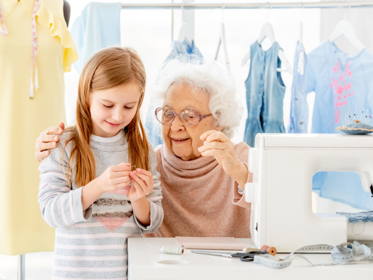 Uroma und Enkeltochter sitzen vor einer N&auml;hmaschine und n&auml;hen