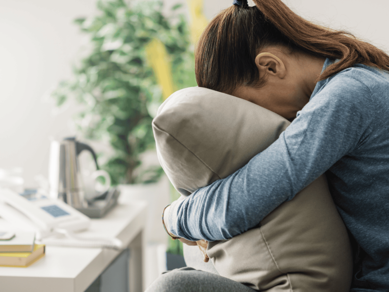 Frau auf dem Sofa drückt ihr Gesicht frustriert in ein Kissen