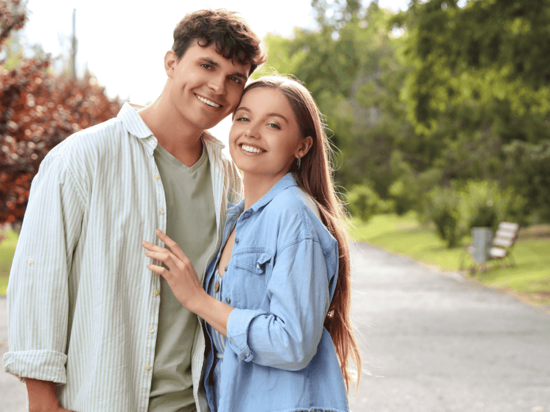 Frau und Mann in der Natur umarmen sich seitlich und schauen lächelnd in die Kamera