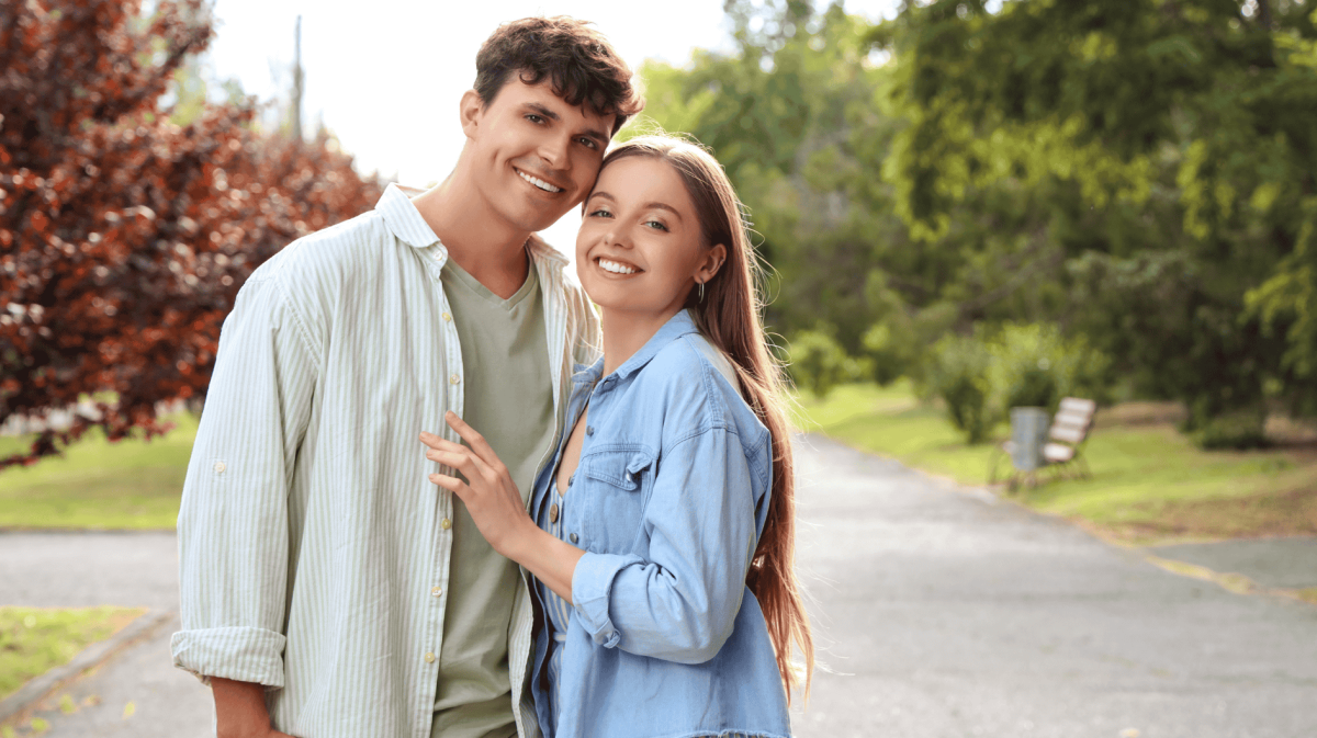 Frau und Mann in der Natur umarmen sich seitlich und schauen lächelnd in die Kamera