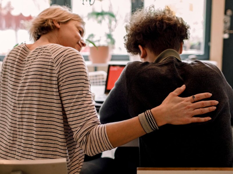 Mutter sitzt neben ihrem Teenager zu Hause und streichelt ihm den Rücken.