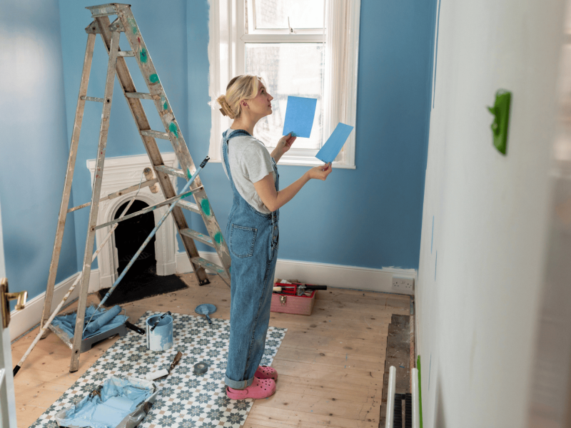 Junge Frau steht in ihrer Wohnung und streicht sie blau.