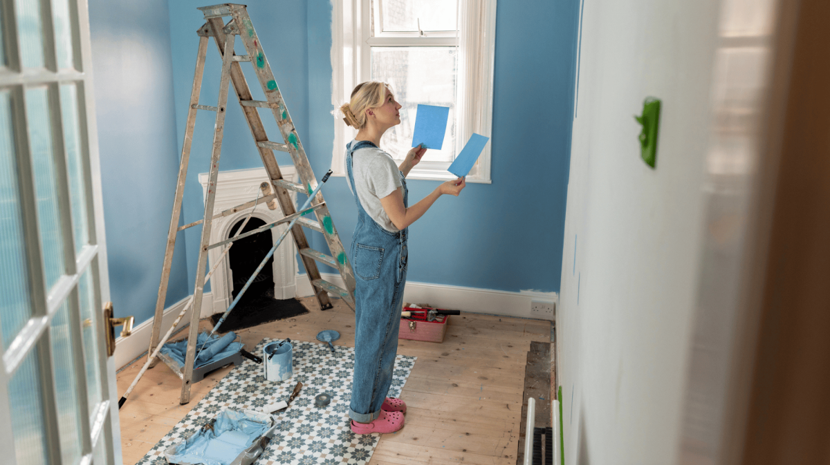 Junge Frau steht in ihrer Wohnung und streicht sie blau.
