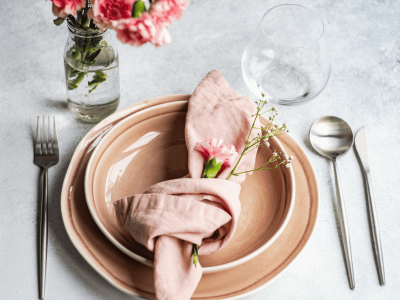 Rosa Geschirr auf grauem Tisch, mit rosa Serviette.