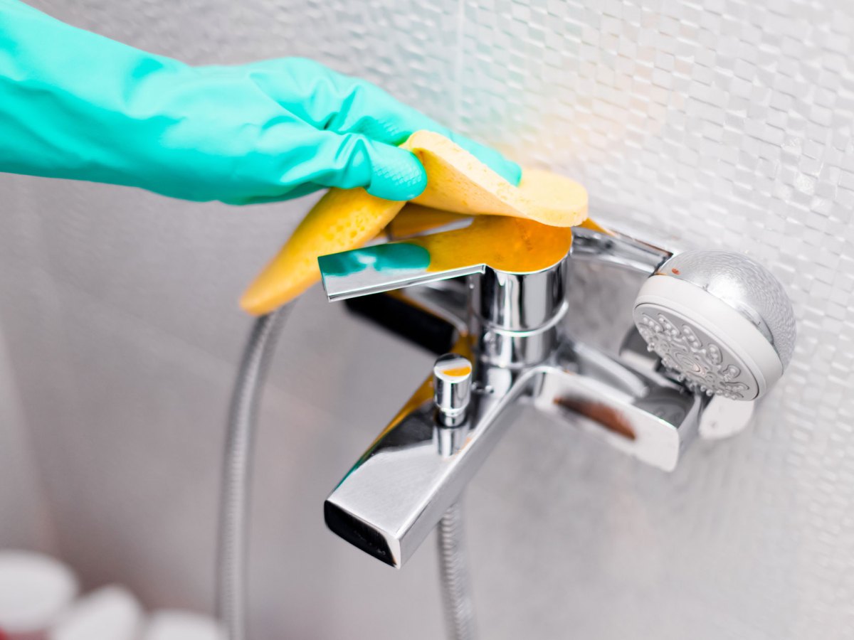 Hand mit Putzhandschuhen in T&uuml;rkis reinigt Armatur
