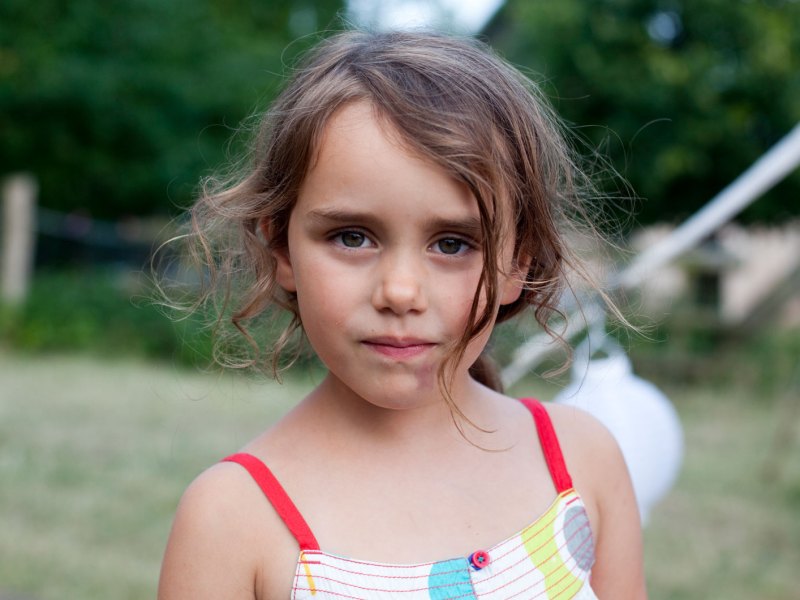 Porträt eines jungen Mädchens, das ernst in die Kamera schaut, während es vor einem Spielplatz steht.