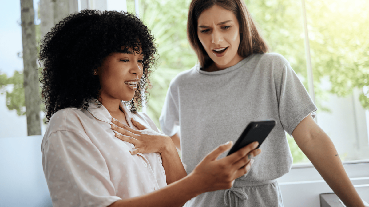 Zwei junge Frauen schauen schockiert auf ein Handy.