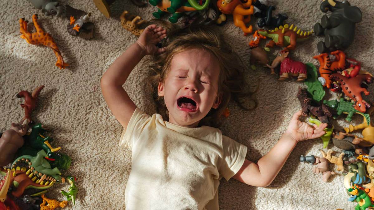 Kind liegt auf dem Teppich, umgeben von Dino-Spielfiguren und weint bitterlich.