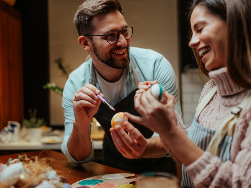 Mann und Frau bemalen Ostereier und lachen gemeinsam