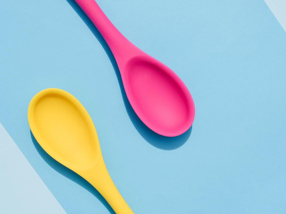 ein pinker und ein gelber Plastiklöffel liegen auf einer blauen Unterlage.