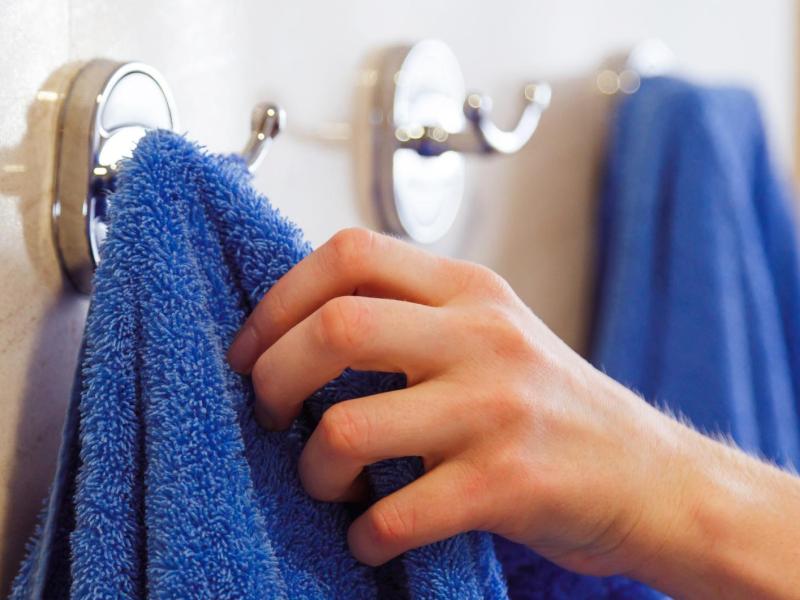 Frau nimmt ein blaues Dusschhandtuch vom Haken.
