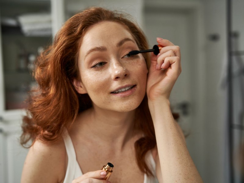 Frau, die sich mit einer Wimperntusche die Augen schminkt.