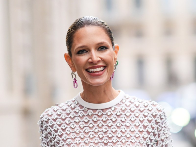 Frau mit einem Designer-Kleid und schicken Ohrringen, die in die Kamera lächelt.