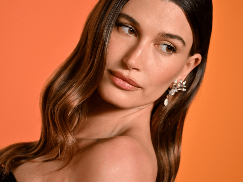 Hailey Bieber posiert in Bandeaukleid vor knalligem Hintergrund