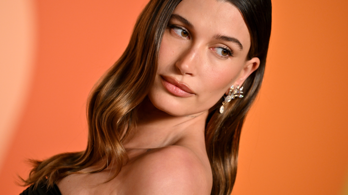 Hailey Bieber posiert in Bandeaukleid vor knalligem Hintergrund