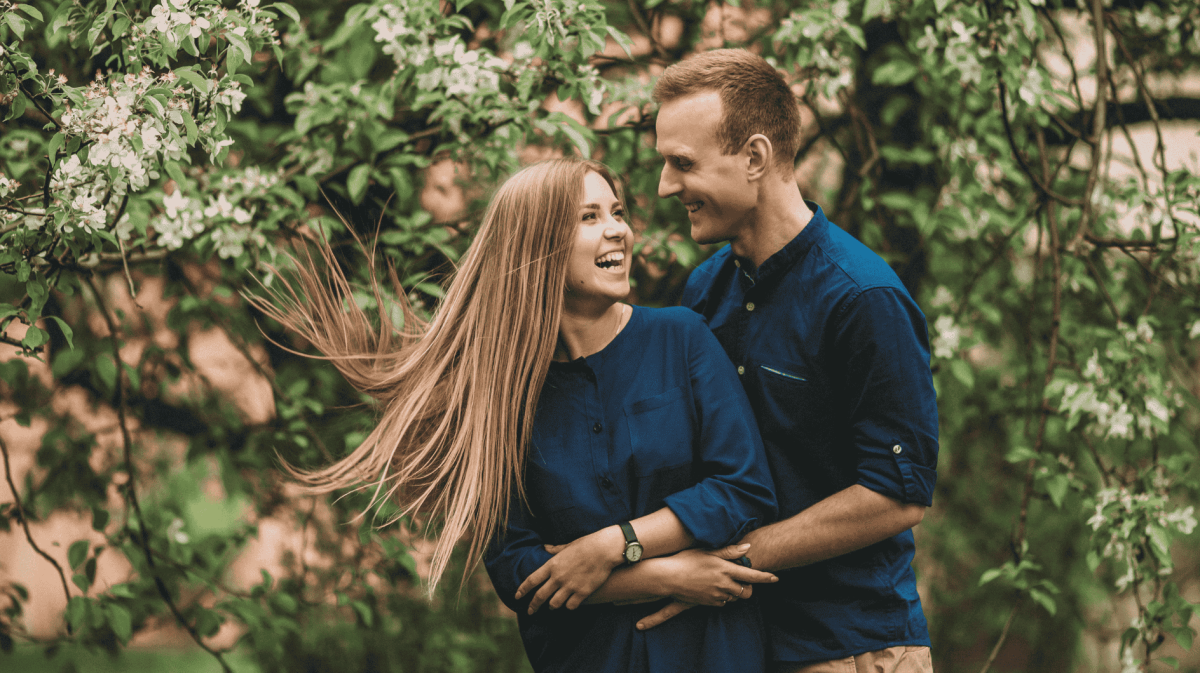Frau und Mann vor einem blühenden Baum lachen und halten sich in den Armen