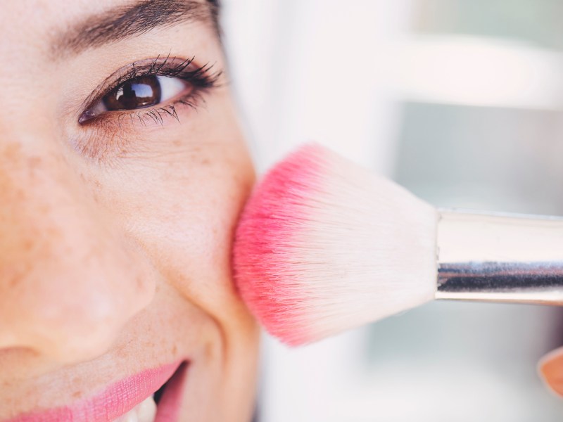 Frau trägt sich mit einem Pinsel Rouge auf.
