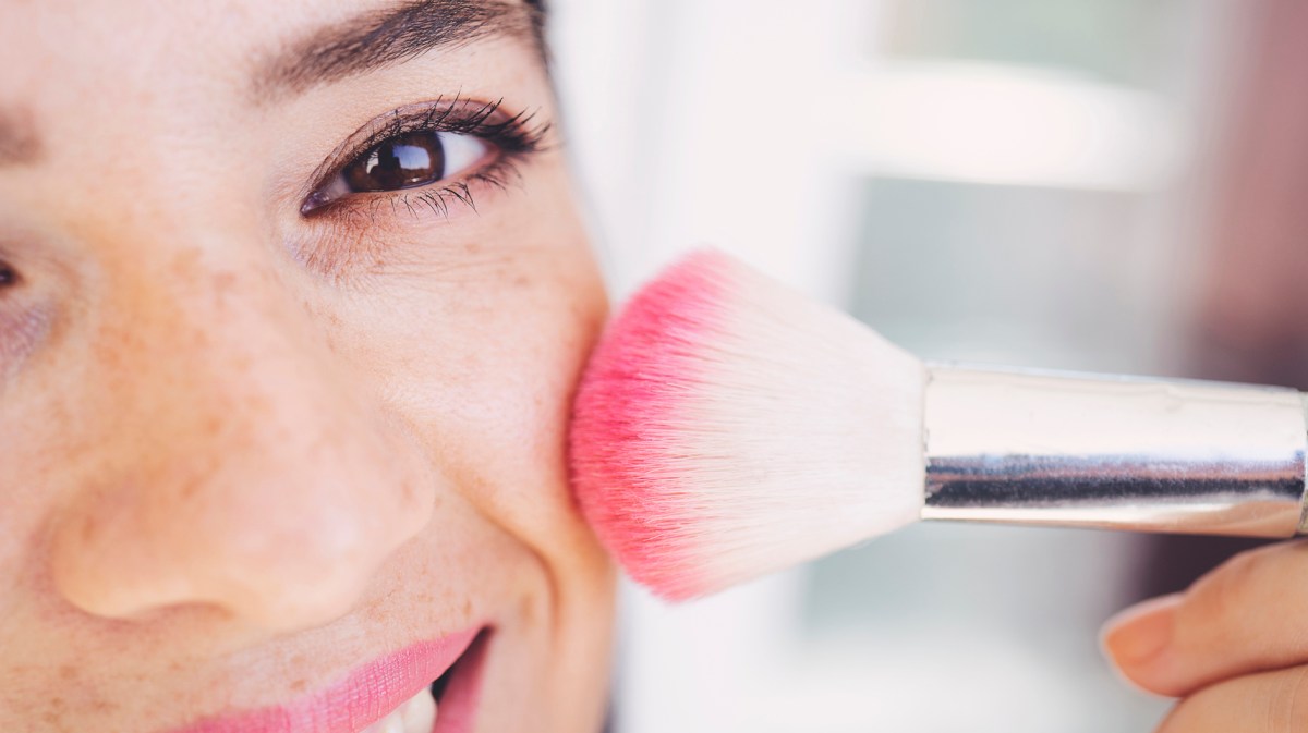 Frau trägt sich mit einem Pinsel Rouge auf.
