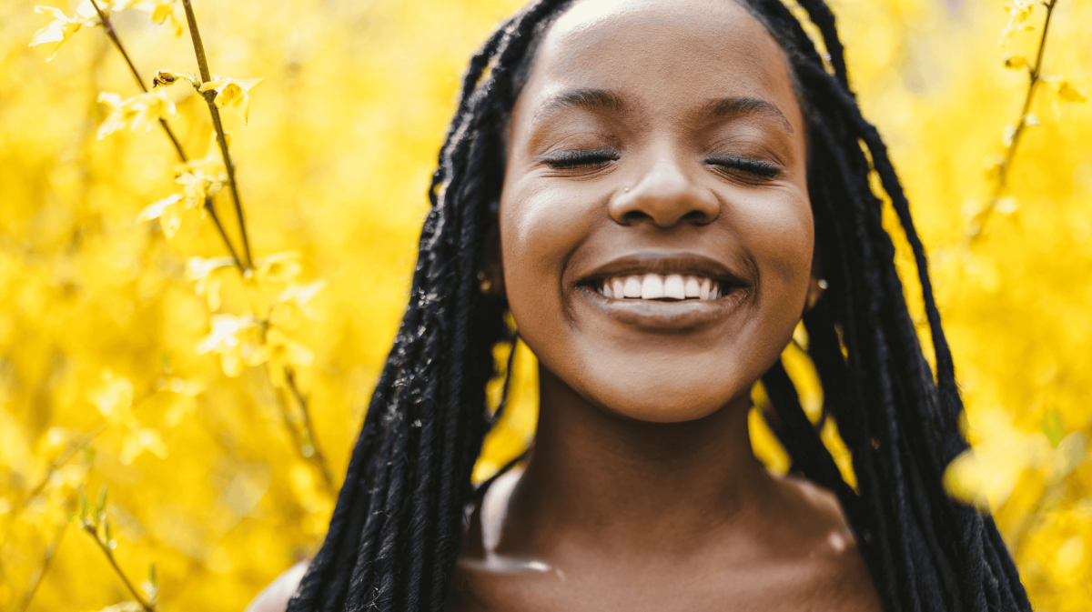 Frau umgeben von gelben Blumen lächelt mit geschlossenen Augen in die Kamera
